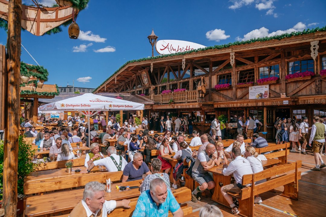 Aussenansicht der Almhütte Royal. Die Menschen sitzen im Biergarten vor der Hütte und genießen das gute Wetter.