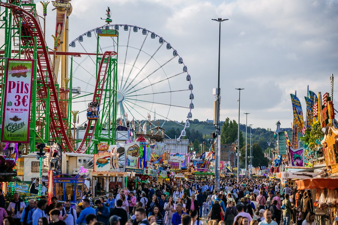 Unzählige Menschen auf dem Festplatz. Links sind mehrere Fahrgeschäfte, darunter die Wilde Maus XXL und das Riesenrad. 