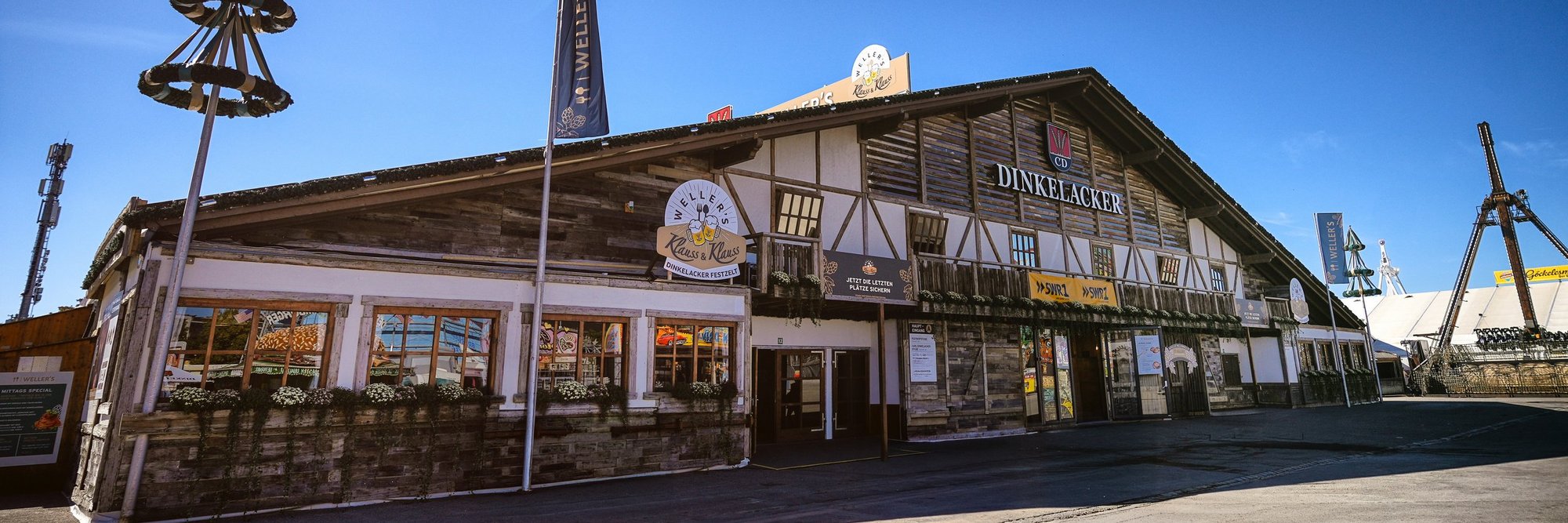 Das Weller's Klauss und Klauss Dinkelacker Festzelt in der Frontal-Ansicht bei strahlend blauem Himmel