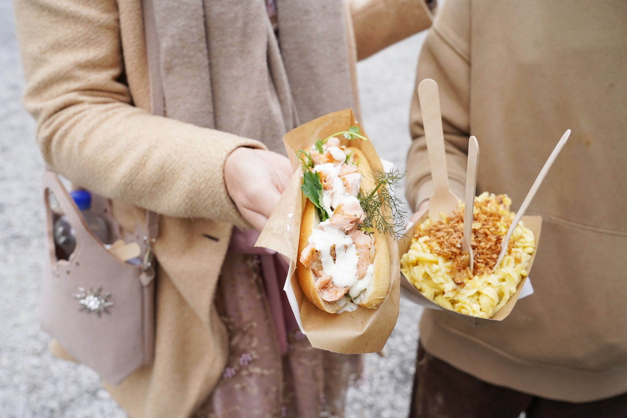 Zwei Frauen halten ein Lachsbrötchen und eine Portion Käsespätzle in den Händen.