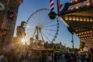 Abendliche Stimmung auf dem Volksfest. Die Sonne geht hinter der Geisterbahn unter, daneben wird das Riesenrad von der Sonne noch angestrahlt.