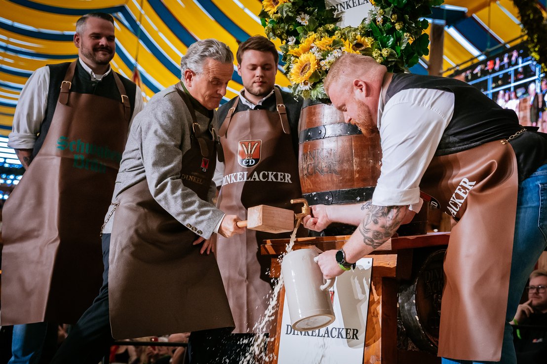Der Oberbürgermeister schläft das Bierfass an. Bier fließt aus dem Zapfhahn. Braumeister hält Bierkrug und Hahn fest.