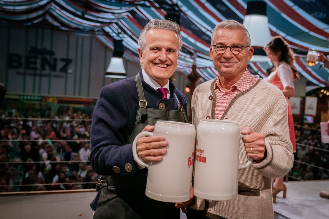 [Translate to English:] Stuttgarts Oberbürgermeister Frank Nopper und Innenminister Thomas Strobl stoßen nach dem Fassanstich im Festzelt "Beim Benz" mit ihren Ton-Maßkrügen an und blicken freudig in die Kamera