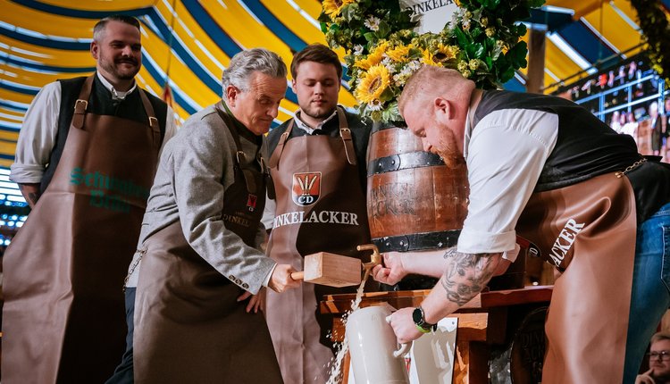 Der Oberbürgermeister schläft das Fass an. Bier fließt in einen Krug. Braumeister hält den Krug und den Zapfhahn..