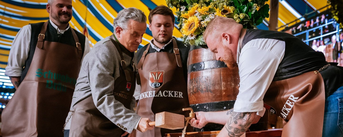 Der Oberbürgermeister schläft das Fass an. Bier fließt in einen Krug. Braumeister hält den Krug und den Zapfhahn..