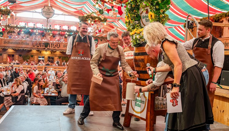 Der Oberbürgermeister schlägt das Bierfass an, aus dem Bier fließt. Der Braumeister hält den Krug.