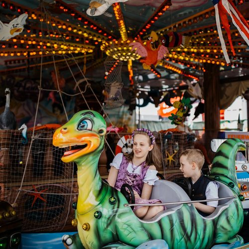Zwei Kinder sitzen auf einem Fabelwesen in einem Karussell