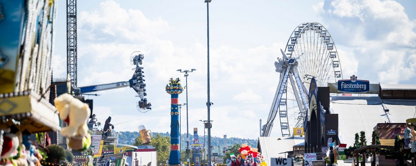 Blick über Feststraße auf Fruchtsäule, Riesenrad, Fahrgeschäfte und viele Menschen.