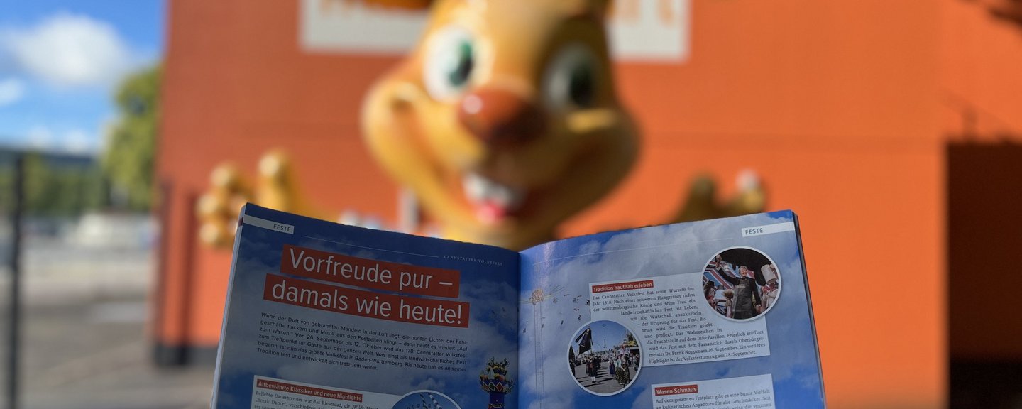 Das neue Live-Magazin Ausgabe Herbst 2025 aufgeschlagen beim Artikel zum Volksfest. Im Hintergrund steht eine große Wasen-Hasi-Figur.