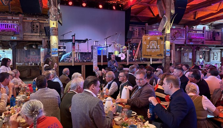 Vor der Bühne hinten im Bild steht Bürgermeister Thomas Fuhrmann. Davor sitzen an den Biertischen Schaustellerinnen und Schausteller und frühstücken.