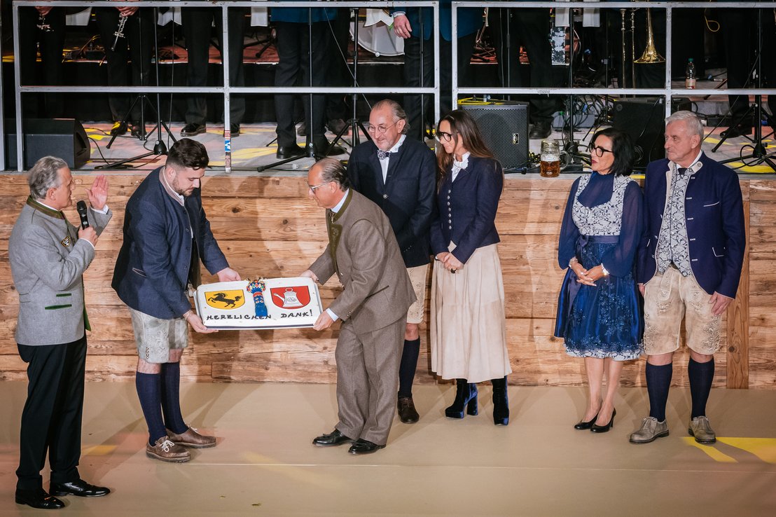 OB dankt Brüdern Klauss. Torte mit Stuttgarter und Cannstatter Wappen und Fruchtsäule darauf wird gehalten. Brüder Klauss mit Ehefrauen schauen zu Torte.