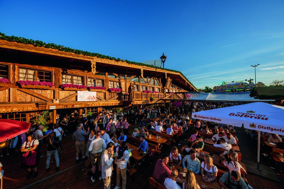 Außenansicht der Almhütte Royal bei Sonnenuntergang. Die Menschen sitzen im Biergarten vor der Hütte und genießen die gute Stimmung.